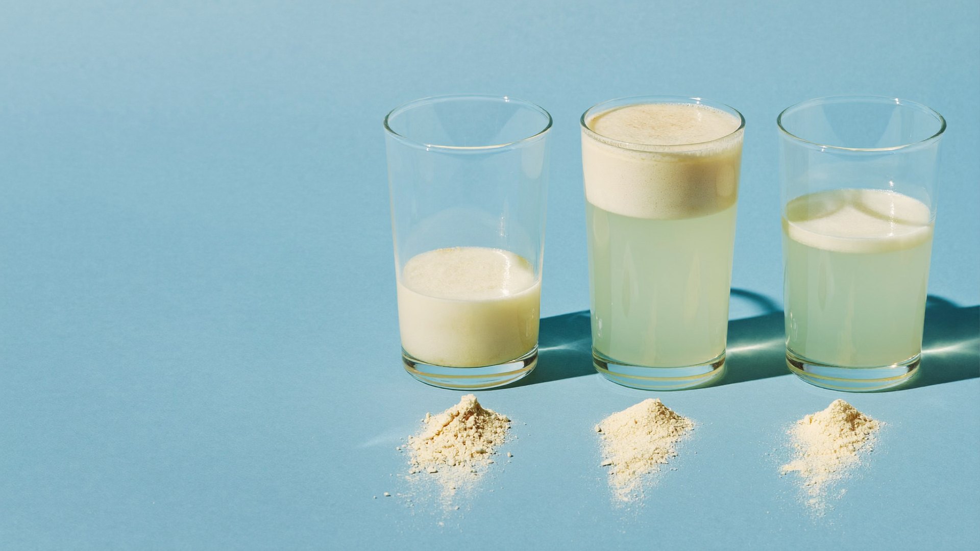 Three glasses of supplement drink filled to different levels, a heap of powder in front of each