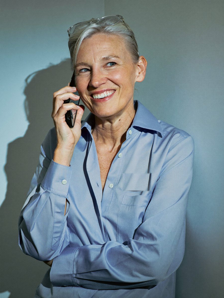 A scientist laughing on a phone call against a blue-grey wall