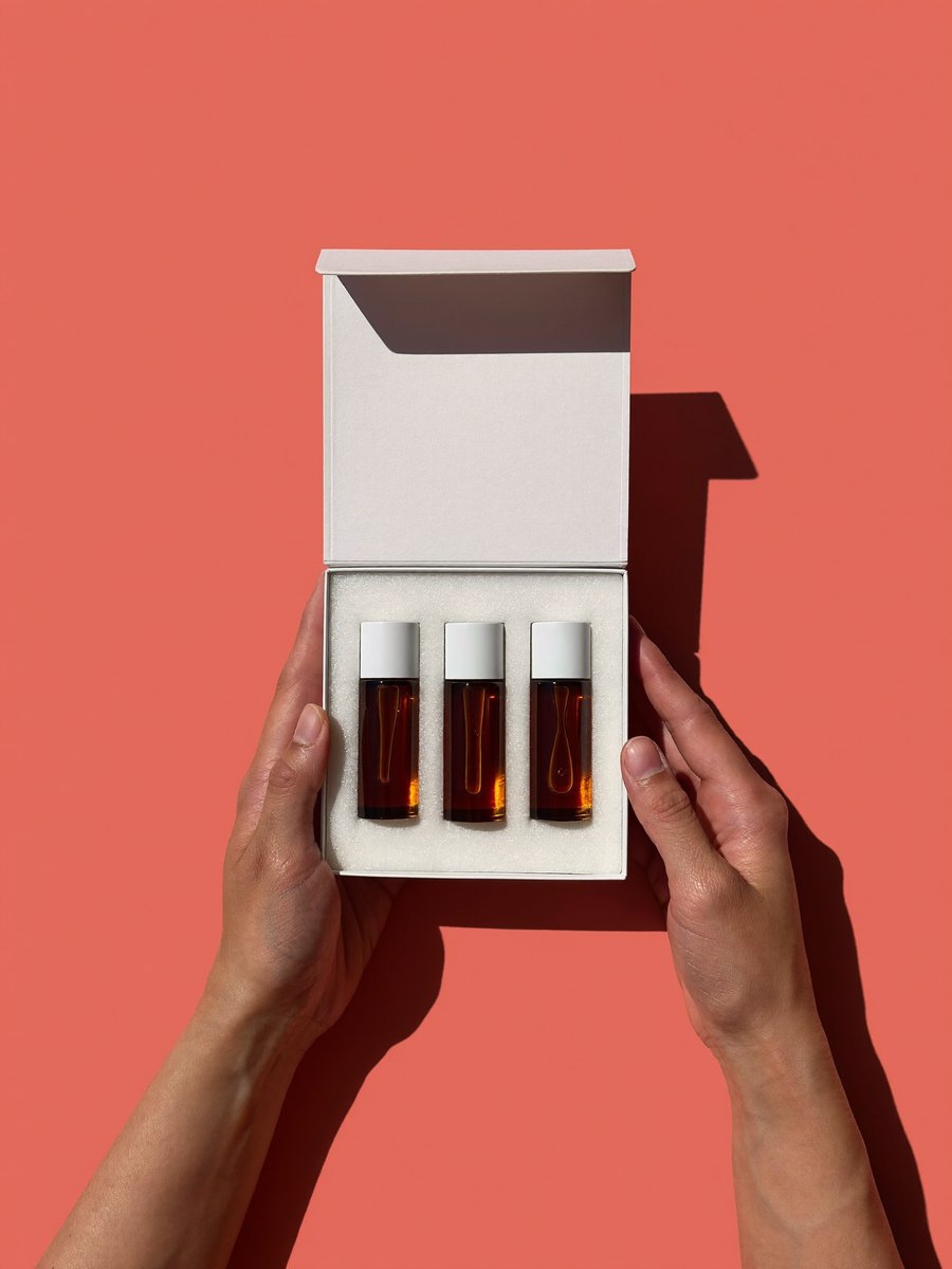 Hands holding an open box of three amber sample vials on a coral ground