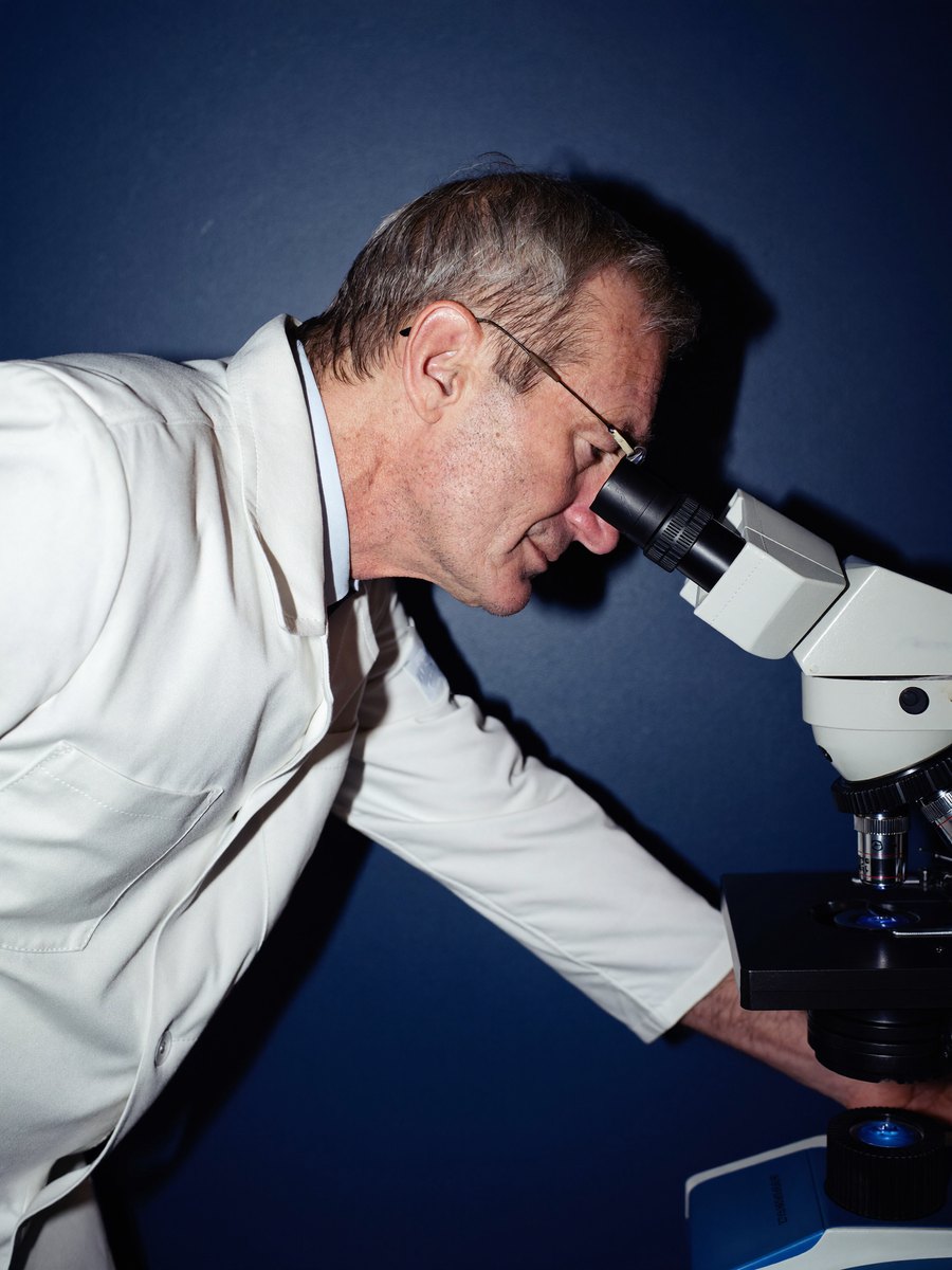 A scientist looking through a microscope against a navy wall