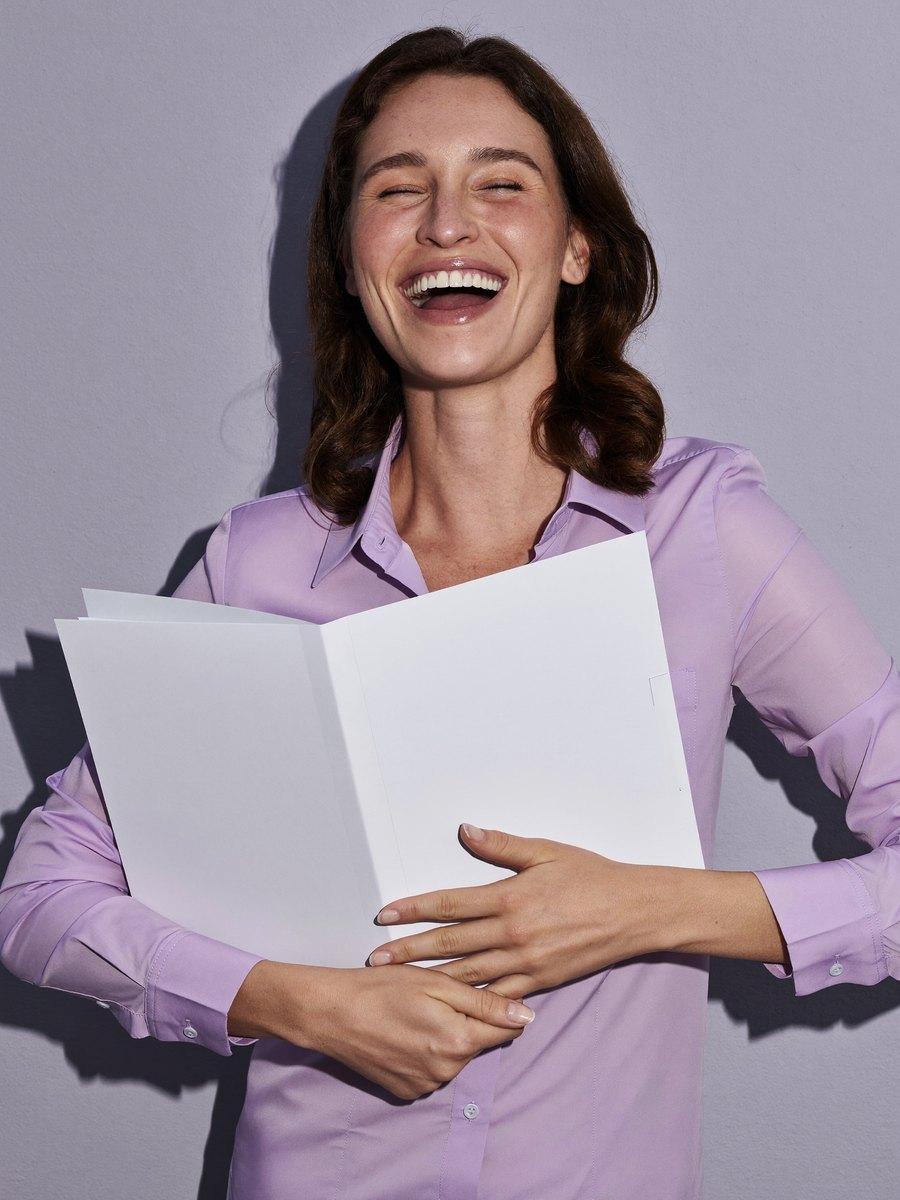 A woman smiling with a white folder held to her chest