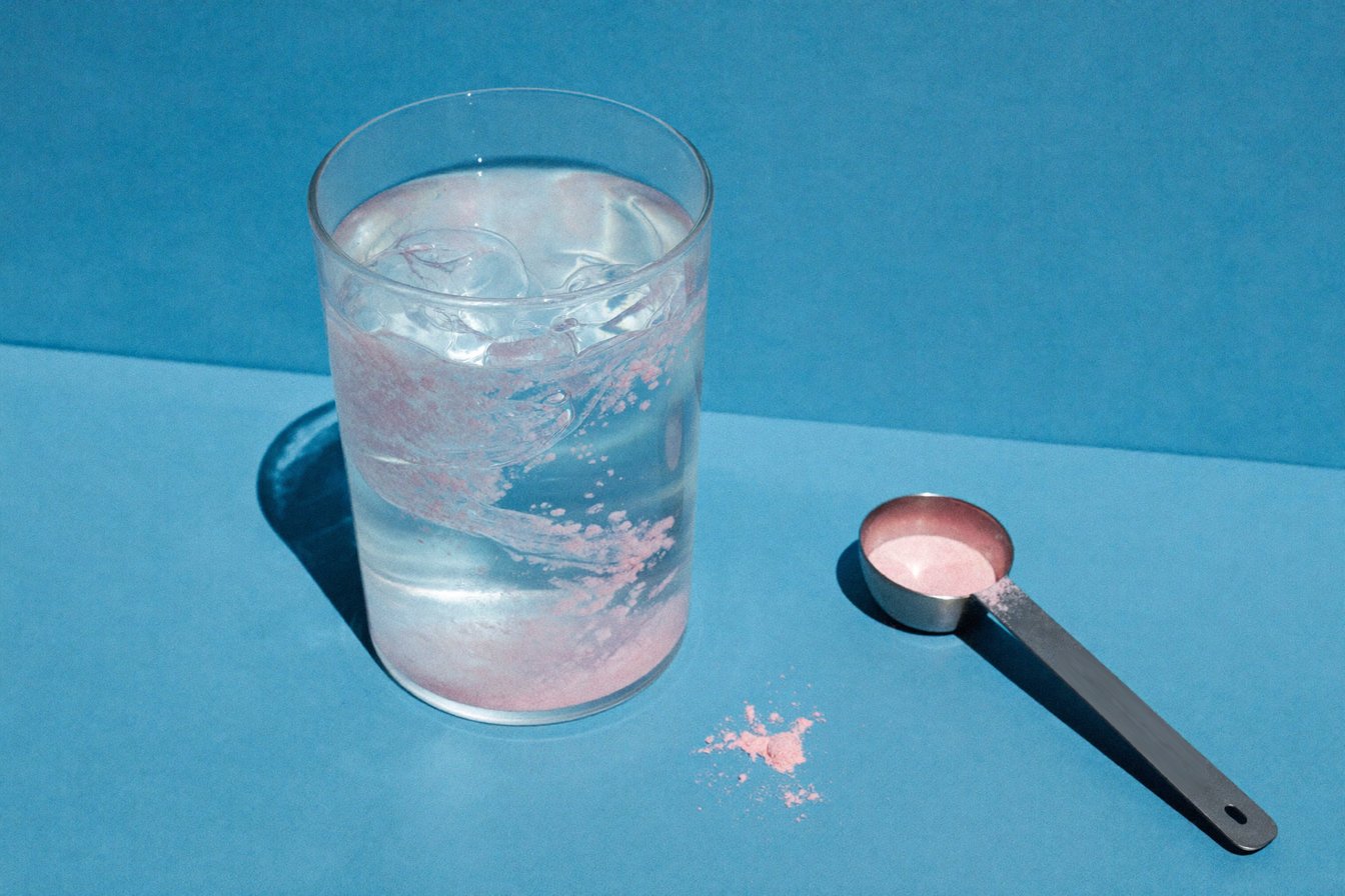 Pale pink electrolyte powder dissolving in a glass of water beside a steel scoop