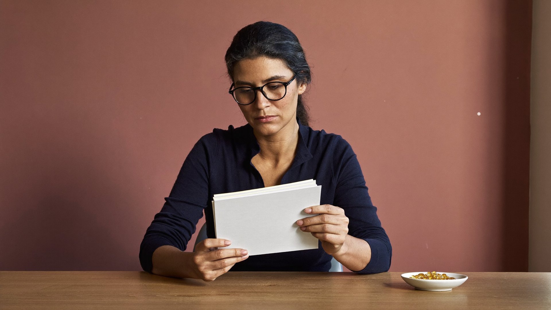 A scientist at a desk reading a short stack of papers, a dish of softgels beside her