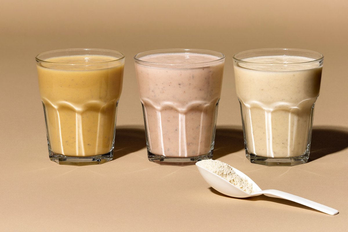 Three protein shakes side by side with a scoop of powder