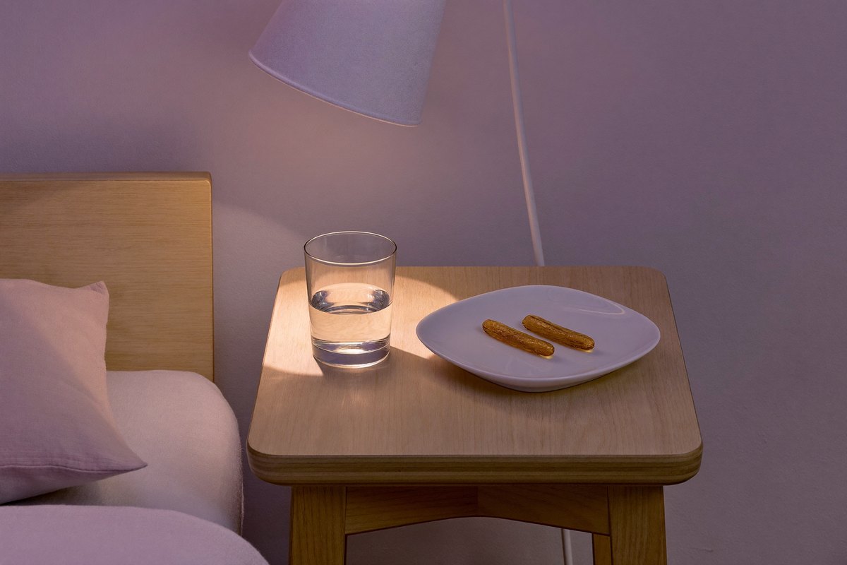 A bedside table at dusk with a glass of water and two softgels