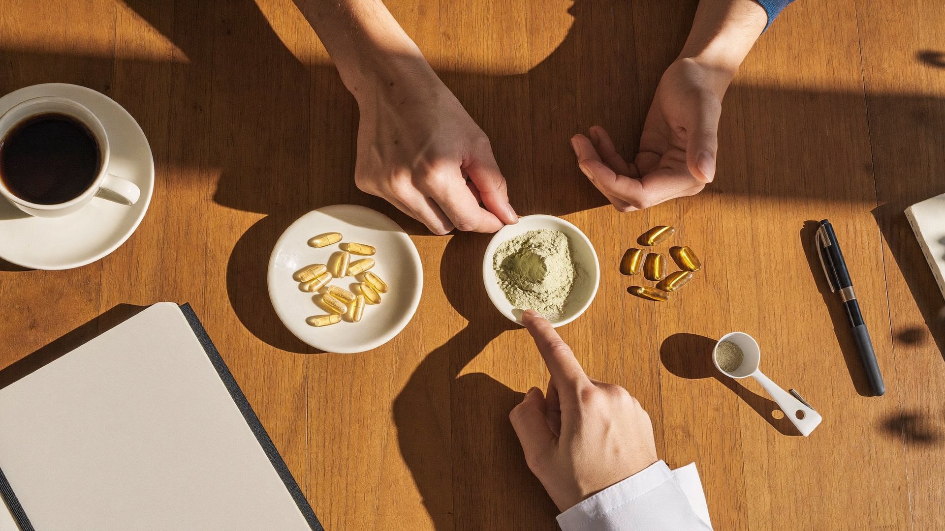 A founder and a scientist at a sunlit table with softgels, powder and a scoop between them