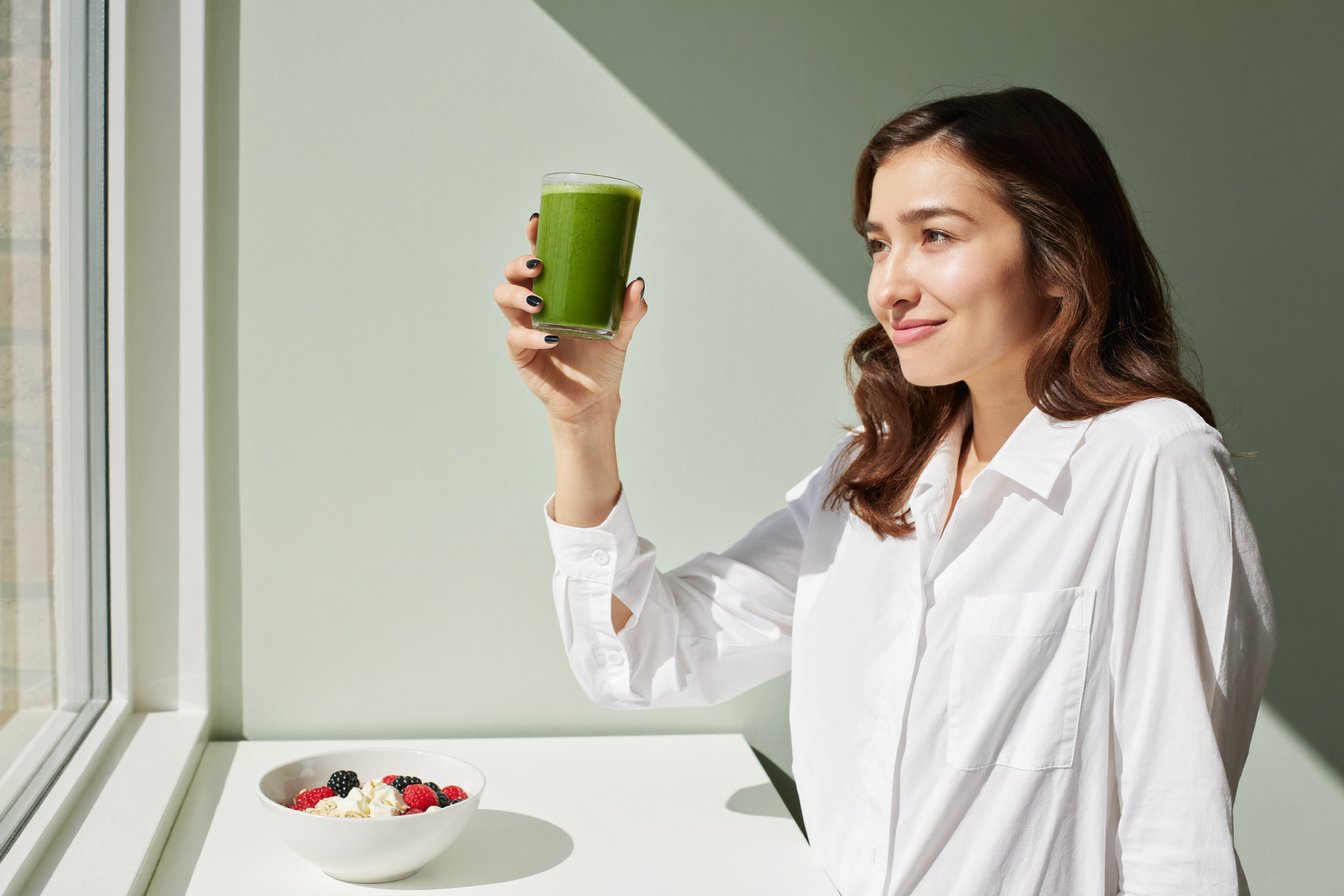 A product developer holding up a glass of a bright green functional drink in a test kitchen
